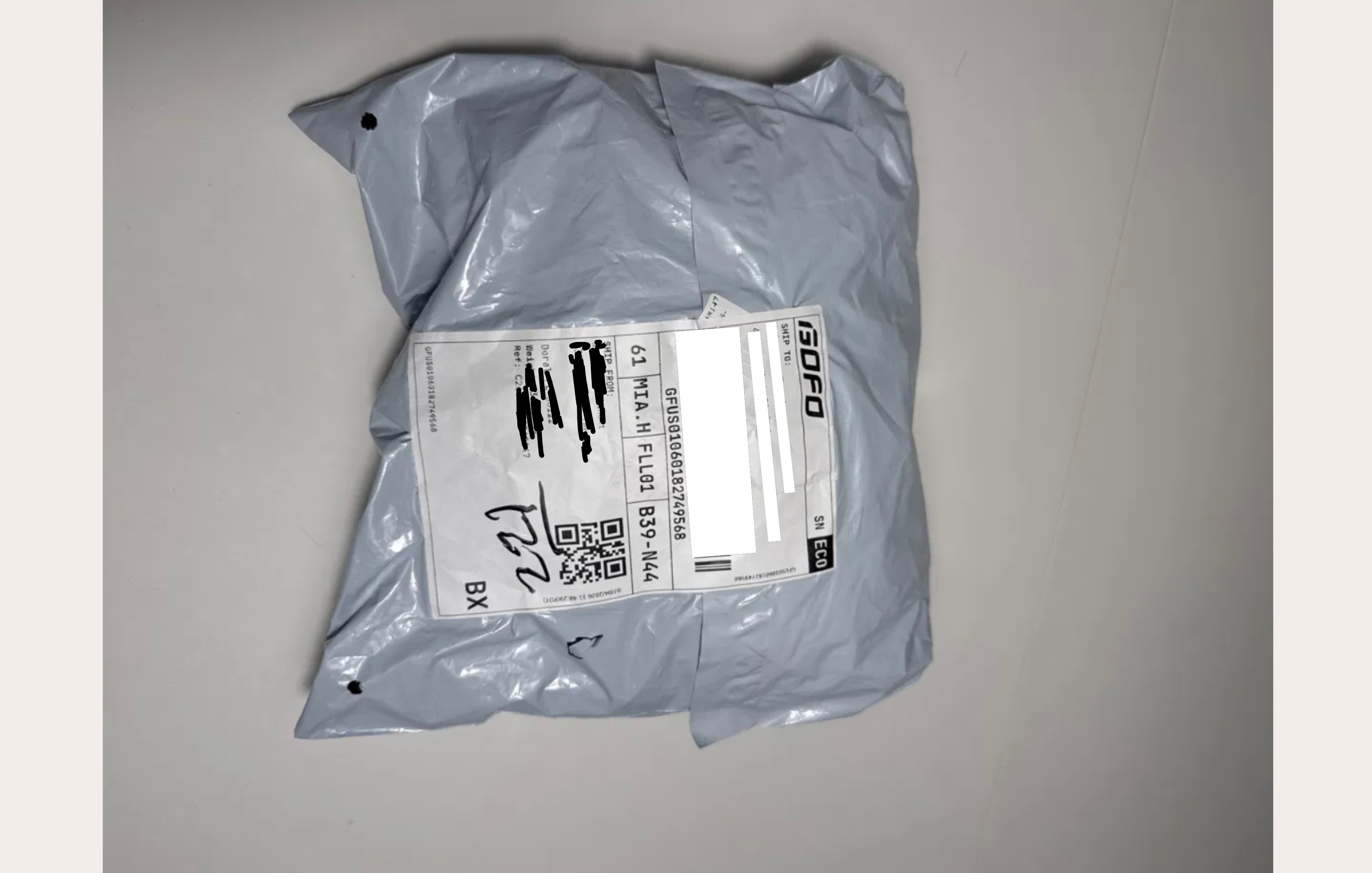 Gray poly mailer with ISOFO carrier shipping label — no brand identity, crumpled from transit