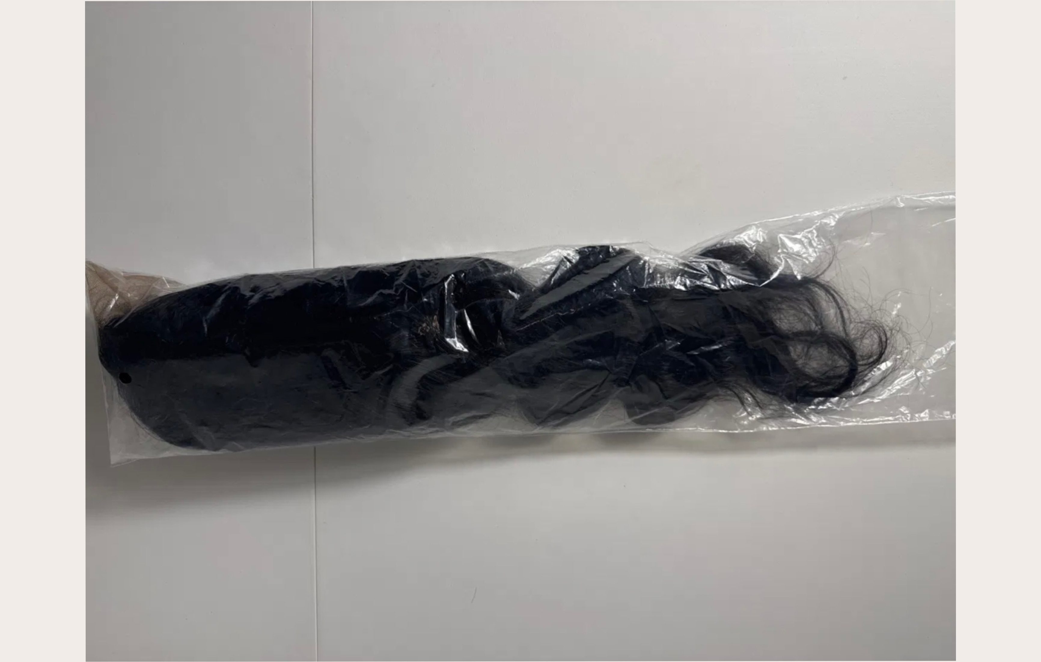 Wig compressed in clear plastic bag — hair escaping at the top, lace folded, no internal structure